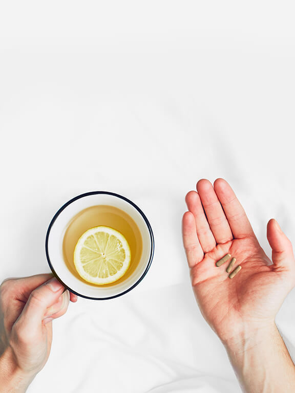 Man holding a cup of tea with a lemmon slice, and a dose of YouVeda's supplement